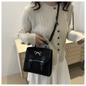 Detailed view of a black handbag with red heart patterns and a silver bow on a model