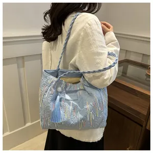 Detail of light blue embroidered tote bag with woven strap and side tassel fringe accent