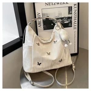 Gros plan sur un sac à bandoulière blanc avec papillon en métal et breloque ours en peluche