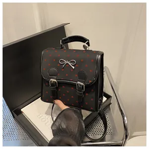 Close-up of black backpack with red heart prints and silver bow on luxury book