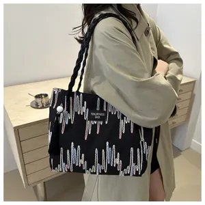 Detail of black tote bag with colorful wave embroidery and woven handle on person