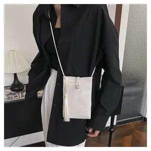 Détail du mini sac bandoulière crème avec texture jacquard et pompon en soie élégant