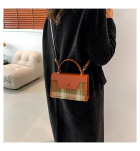 Détail d'un sac bandoulière en cuir et tissu à carreaux avec un long manteau noir