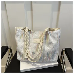 Close-up of white embossed tote bag with colorful embroidery and woven rope handle