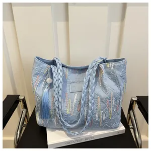 Light blue tote bag with colorful wave embroidery and woven handle detail on a white book