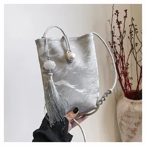 Détail du mini sac en soie argentée avec motif marbre, fermoir perle et glands longs