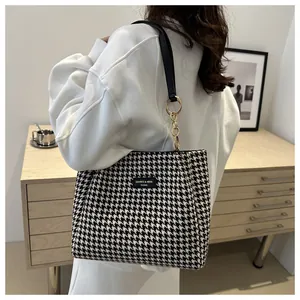 Détail du sac cabas pied-de-poule avec chaîne dorée et étiquette en cuir sur modèle