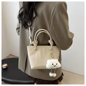 Dettaglio borsa a secchiello beige con manico a nodo e ciondolo a nuvola su modella