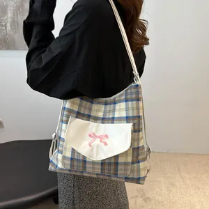 Blue and yellow plaid tote bag with pink bow embroidery and white pocket worn by a model