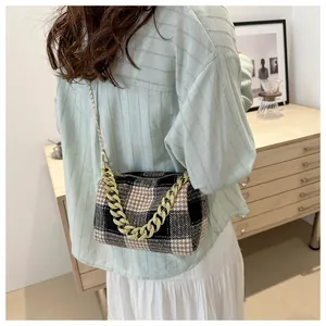 Détail du sac oreiller à carreaux avec chaîne dorée porté par un mannequin en intérieur