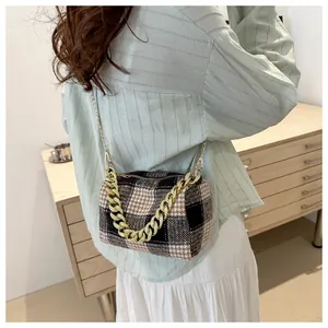 Vue détaillée d'un sac cylindrique à carreaux avec chaîne dorée sur meuble en bois