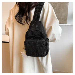Detail of black pleated crossbody bag with plush charm on a cream dress outfit