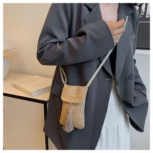 Détail d'un sac de téléphone en paille tressée avec boucle dorée et longues franges