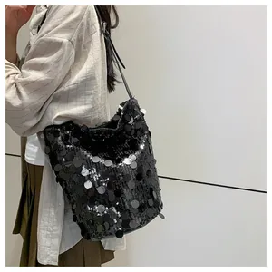 Dettaglio di una borsa a secchiello con paillettes nere e tracolla in pelle su un abito