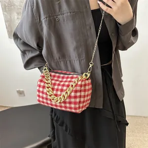 Sac bandoulière cylindrique à carreaux rouge et blanc avec chaîne dorée porté par un mannequin