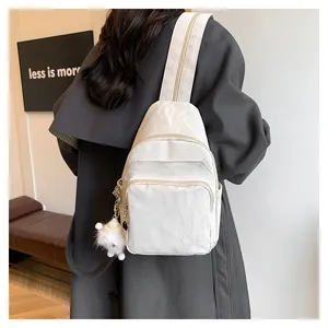 Detail of white pleated texture chest bag with cute plush ball charm and zipper pockets