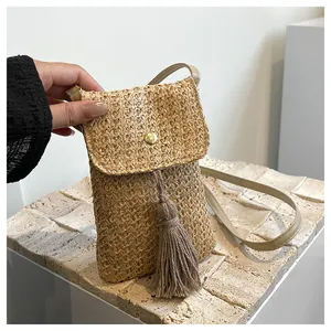Detailed macro view of woven straw phone bag featuring gold snap and tassel fringe detail