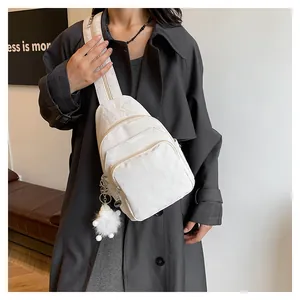 White textured crossbody chest bag featuring glossy pleated fabric and a plush ball charm