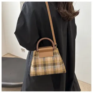 Detail of vintage plaid trapezoid handbag with brown leather handle and metal rivets