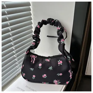Détail d'un petit sac carré noir avec motifs de roses roses et poignée plissée