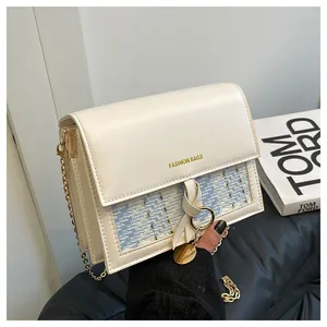 Detail of a square flap bag with beige leather and blue woven texture and gold chain strap