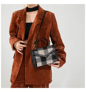 Detailweergave van de geruite enveloptas gedragen door een model in een bruine blazer
