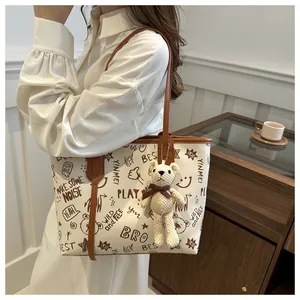 Detail of a beige tote bag with graffiti prints, brown trim, and a cute knitted bear charm