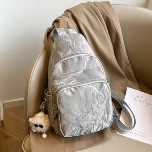 Silver wrinkled multi-pocket crossbody chest bag with plush sheep charm on beige leather seat