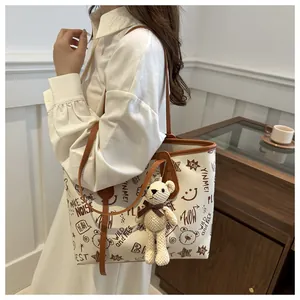 Detail of off-white tote bag with brown graffiti patterns and knit bear charm accessory