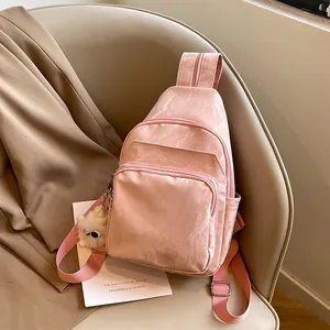 Pink pleated crossbody chest bag with plush charm shown on a stylish cream leather seat