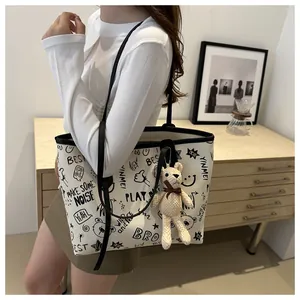 Close-up of a white tote bag with graffiti prints and a cute bear charm in a lifestyle setting