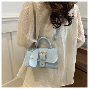 Detail view of light blue crossbody bag featuring a large gold buckle and a mini pouch