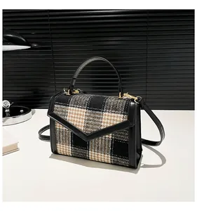 Detail van geruite crossbodytas met V-vormige flap en gouden metalen gesp