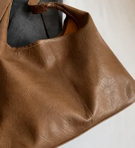 Macro detail of brown leather tote bag showing vintage wrinkled texture and fine stitching