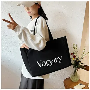 Détail du grand sac cabas en toile noire avec texte Vagary porté par un mannequin