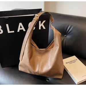 Brown pleated Hobo bag with adjustable strap and gold hardware on a leather sofa