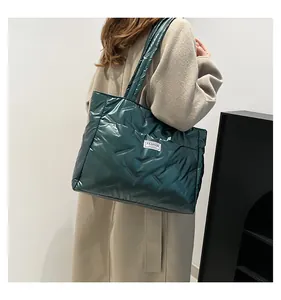 Close-up of a large dark green quilted tote bag with metallic finish and logo patch
