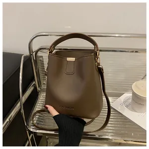 Détail d'un sac seau marron foncé avec ferrures dorées sur un support en métal moderne