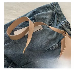 Detail of adjustable shoulder strap and gold buckle on a beige crescent underarm bag