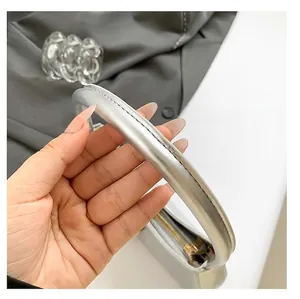 Dettaglio del manico d'argento con trama incrinata e cuciture nere sulla borsa sottobraccio