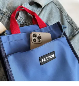 Detail of blue tote bag with red handle featuring a functional phone pocket and fashion label