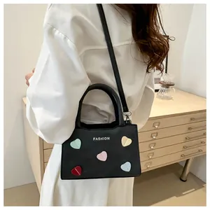 Fashionable black leather handbag with colorful hearts and crossbody strap shown on model