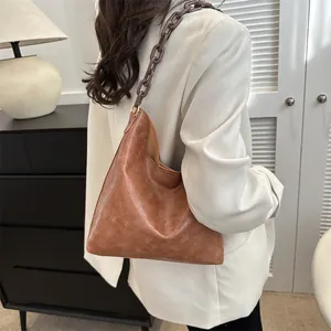 Brown leather tote bag with dark resin chain shoulder strap shown in a home setting