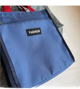 Detail of blue nylon lunch tote bag with red handles and fashion label on front pocket