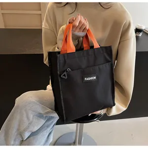 Detail of minimalist black tote bag with orange handles and front zipper pocket