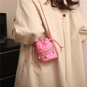 Close-up of pink quilted bucket bag with gold heart charms on model in khaki coat
