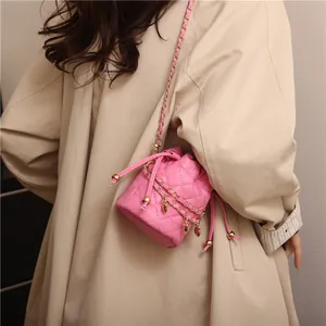 Detail of pink quilted bucket bag with gold heart pendant on khaki trench coat