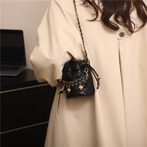 Detail showing black quilted bucket bag with gold chain strap and dangling heart charms