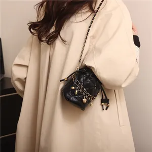 Detailed close-up of a black quilted bucket bag with gold heart charm on a beige coat