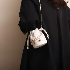Detailed view of white quilted mini bucket bag with gold heart charms on black coat
